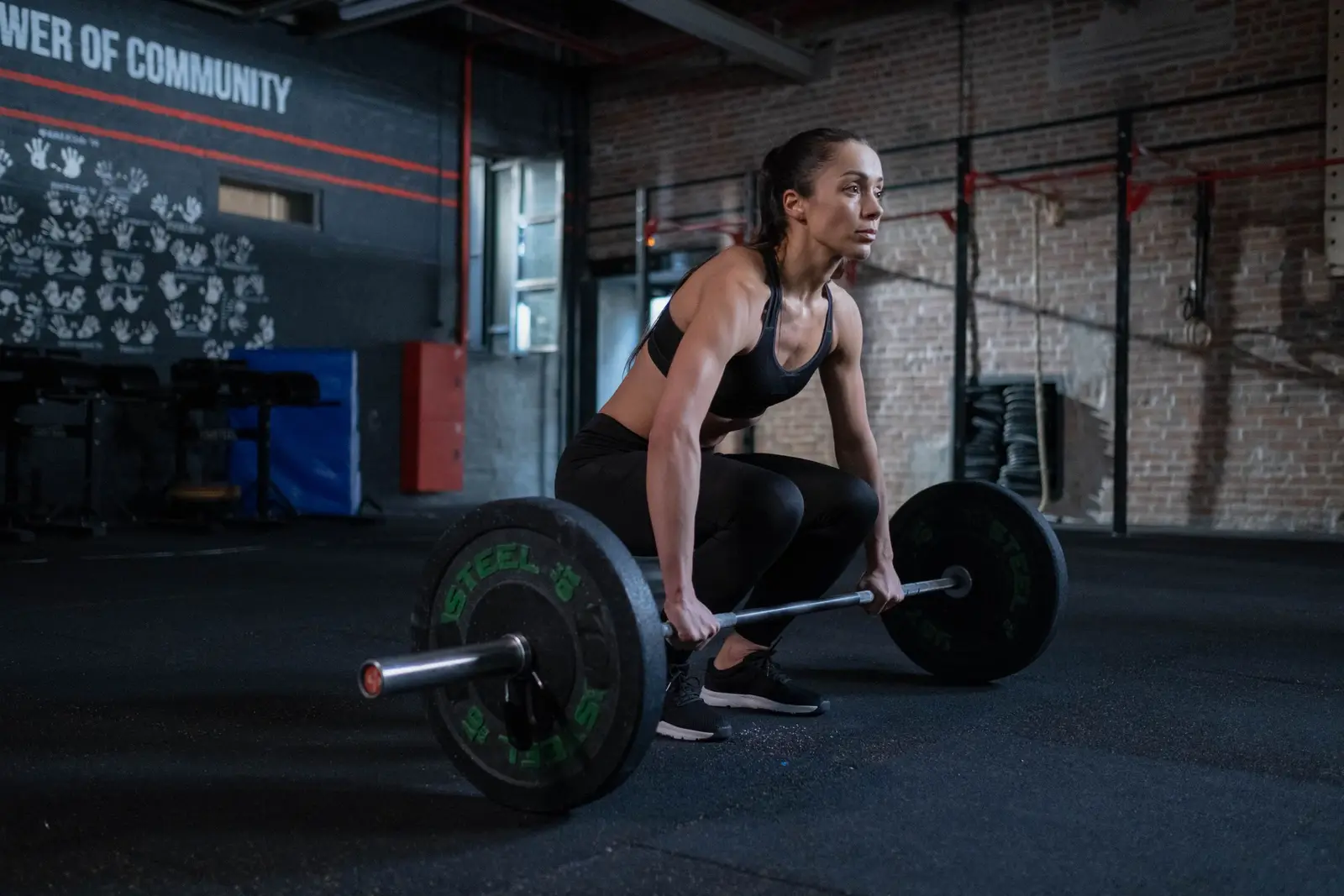 Woman set at a loaded barbell in a dark gym, back flat and arms straight, about to pull